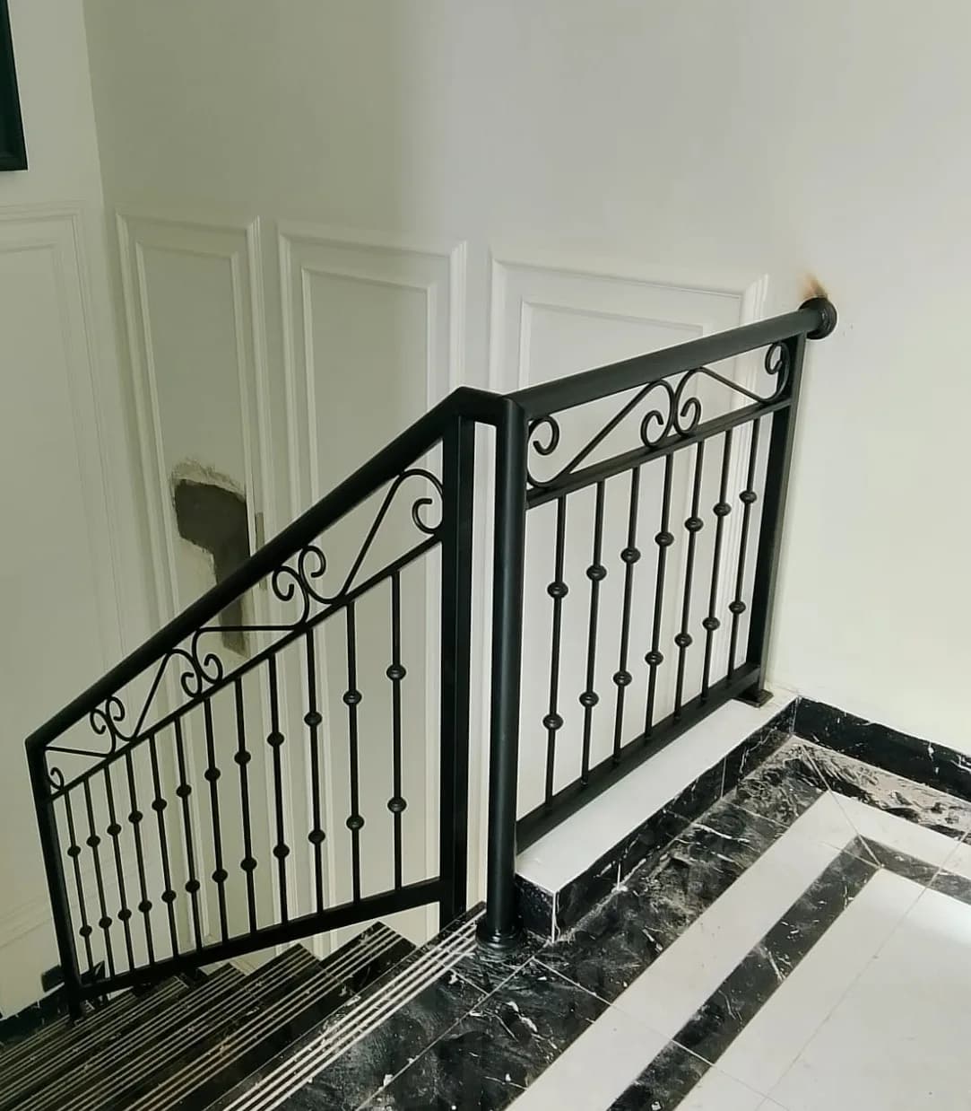 Railing tangga besi hitam motif scroll dengan finishing rapi di dalam rumah